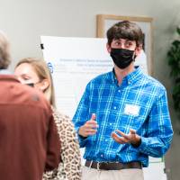 Scholar wearing mask giving poster presentation to another scholar.